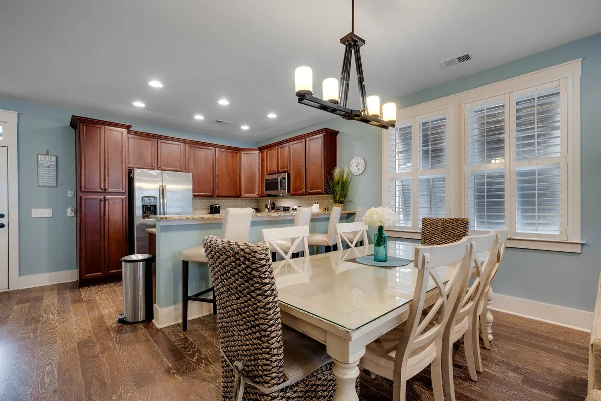 The dining area features a welcoming table set near a kitchen island, illuminated by a stylish light fixture and natural window light. The space feels warm and is ideal for family meals, entertaining guests, or enjoying board games. The kitchen island in the background further enhances the open-plan feel.