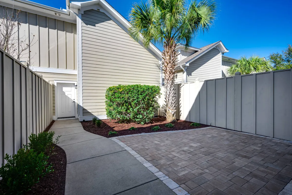 The exterior scene showcases a tranquil backyard with a palm tree, manicured bushes, and a paved pathway, creating a peaceful environment ideal for outdoor relaxation or small gatherings.