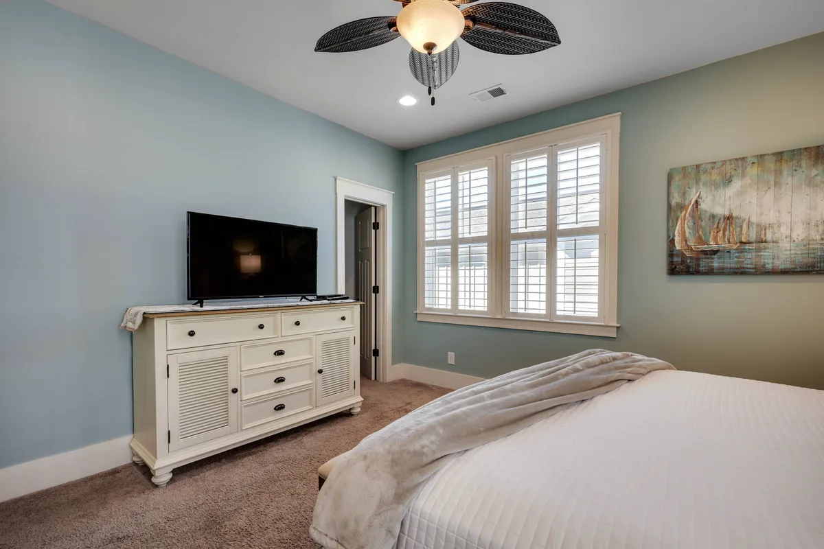 A peaceful bedroom with a neatly made bed, dresser, wall-mounted TV, tasteful artwork, and windows letting in natural light. The overall mood is tranquil and inviting, suggesting a restful place to unwind at the end of the day.