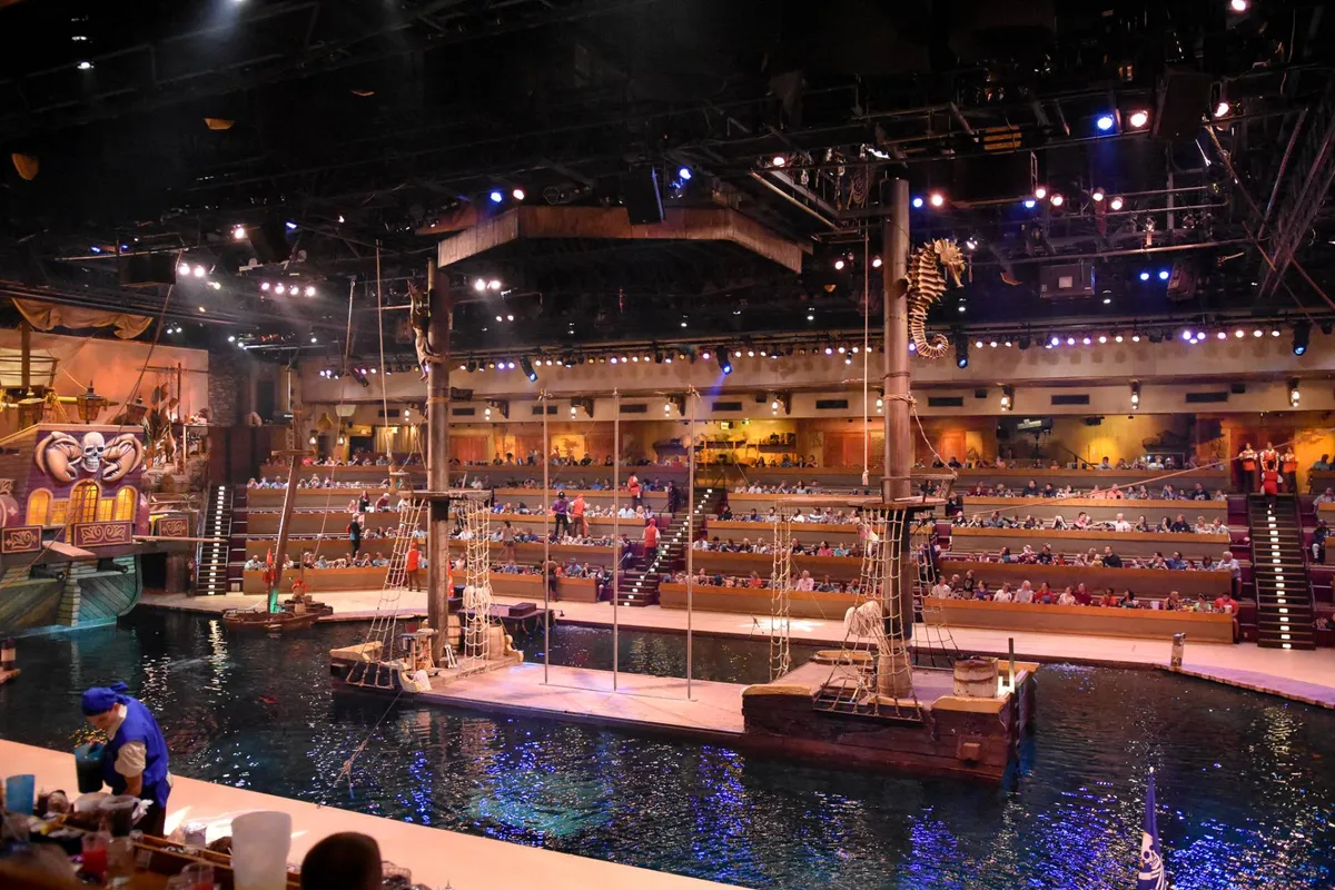 A vibrant scene showcasing a theatrical stage adorned with ships, audience seating, and dramatic lighting. The setting hints at an immersive live performance experience, evocative of the entertainment options couples can enjoy together, such as shows at nearby venues.