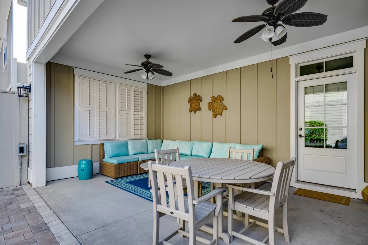 This image features a cozy seating area with plush cushions, a round dining table, decorative wall art, and a door leading outside, allowing for both relaxation and easy indoor-outdoor flow. The natural light and inviting setup evoke a welcoming atmosphere ideal for enjoying coffee or socializing.