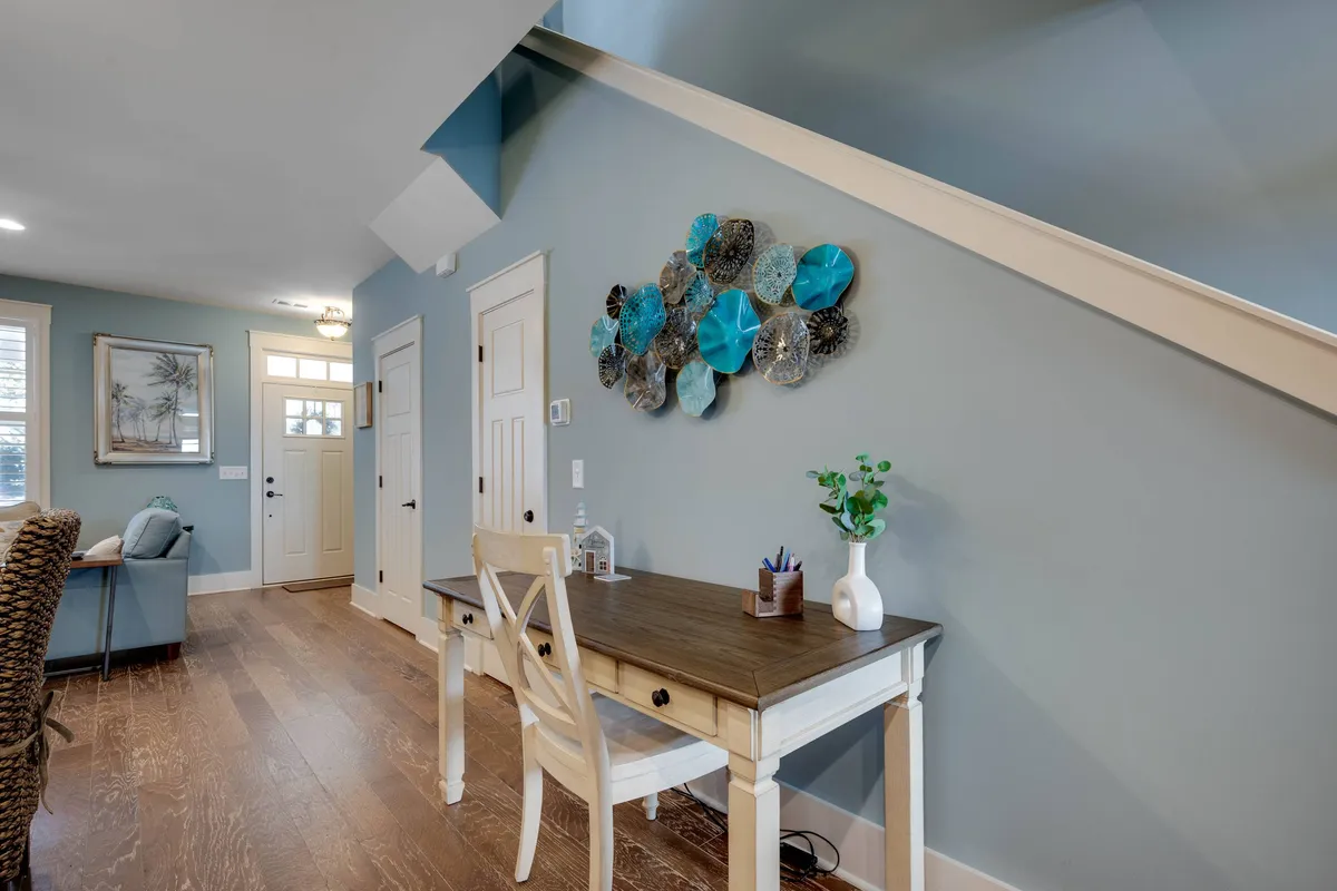 This image features a wooden desk paired with a chair, enhanced by decorative wall art and a green plant. The arrangement is welcoming and intimate, ideal for focused work or creative thinking. Natural light and neat organization create an inviting atmosphere for productivity.